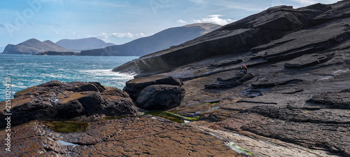 Fotografie Person sitting on dark basalt rocks observing dramatic ocean waves crashing at C