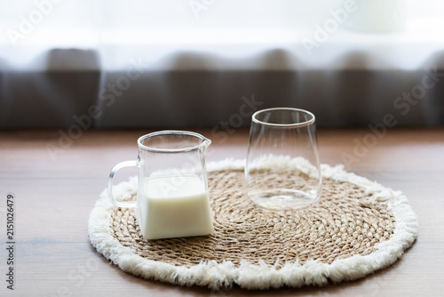 Ingredients for homemade iced coffee preparation with fresh milk and an empty glass on a natural woven placemat. Minimal kitchen scene showing the first step of making a refreshing summer coffee drink