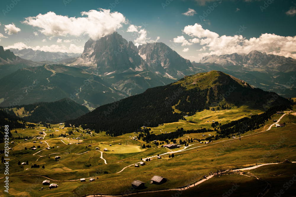 Obraz premium Panoramic view of Sassolungo and Sasso Piatto mountain massif from Seceda in Dolomites, Italy, with green alpine meadows, forested slopes, mountain huts and hiking trails