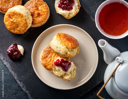 overhead view of scones with jam cream tea and a teapot on a slate background