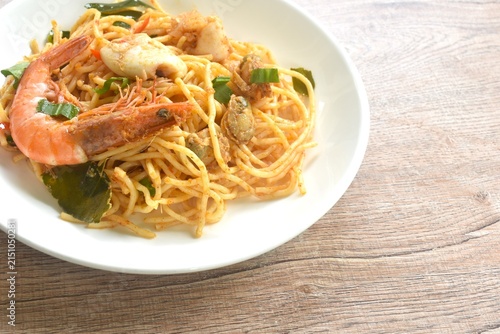 spicy stir fried spaghetti seafood slice squid and shrimp couple clam with chili and basil leaf in Thai tom yum sauce on plate 