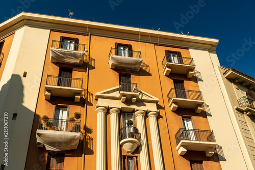 Bari Italy apartment building facade with classical columns and wrought iron balconies in warm orange ochre color under deep blue sky, Mediterranean architecture concept