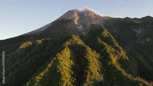 Aerial Footage of Mount Merapi Volcano with Lush Forested Slopes and Its Peak Illuminated by Golden Sunrise Under a Clear Sky. Majestic Volcanic Landscape in Yogyakarta, Indonesia.