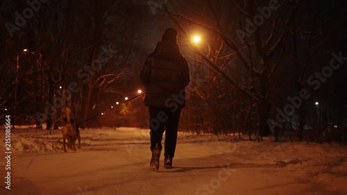 Woman walking her dog on a snowy street of a suburban area at night