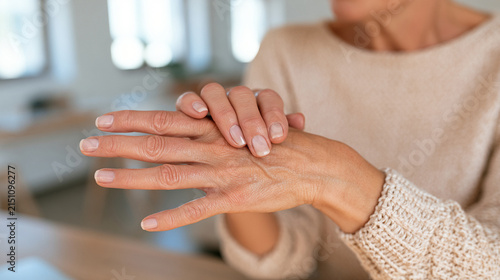 Middle-Aged Woman Massaging Fingers to Relieve Joint Pain and Arthritis in Bright Home Office