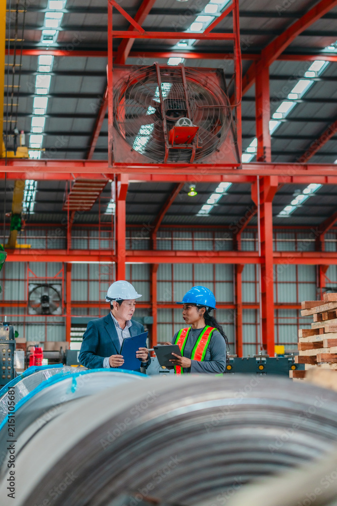 Naklejka premium Manager and female worker discussing over clipboard among steel coils in warehouse factory
