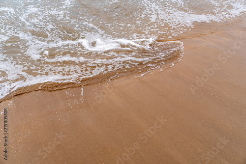 The edge of the ocean where clear water meets the golden sand with gentle foam