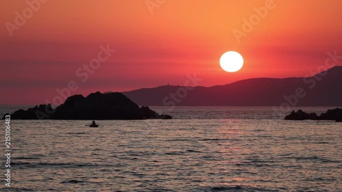 serene sunset over rocky islands in ocean with distant mountains, tranquil view from wide angle shot, relaxing nature scene with orange and red hues, for travel and editorial.