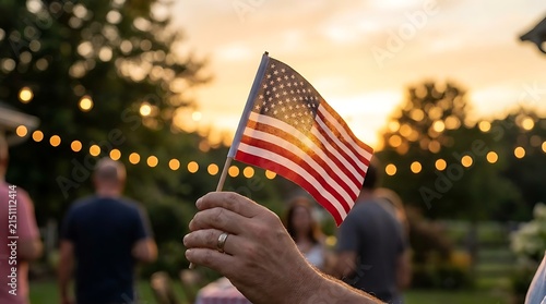 Hand holding American flag at outdoor gathering during sunset