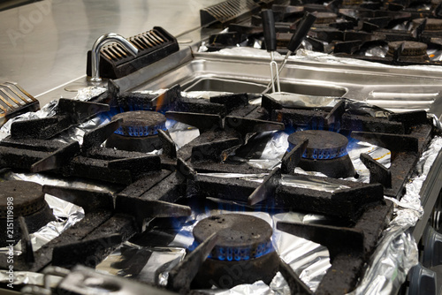 Commercial gas stove burners with blue flames detailed close-up in professional kitchen