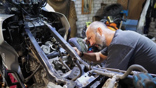 Professional mechanic repairing engine of motorcycle at workshop. Male repairer fixing motor of motorbike using tool at workplace. Adult repairman working at garage. Concept of maintenance service