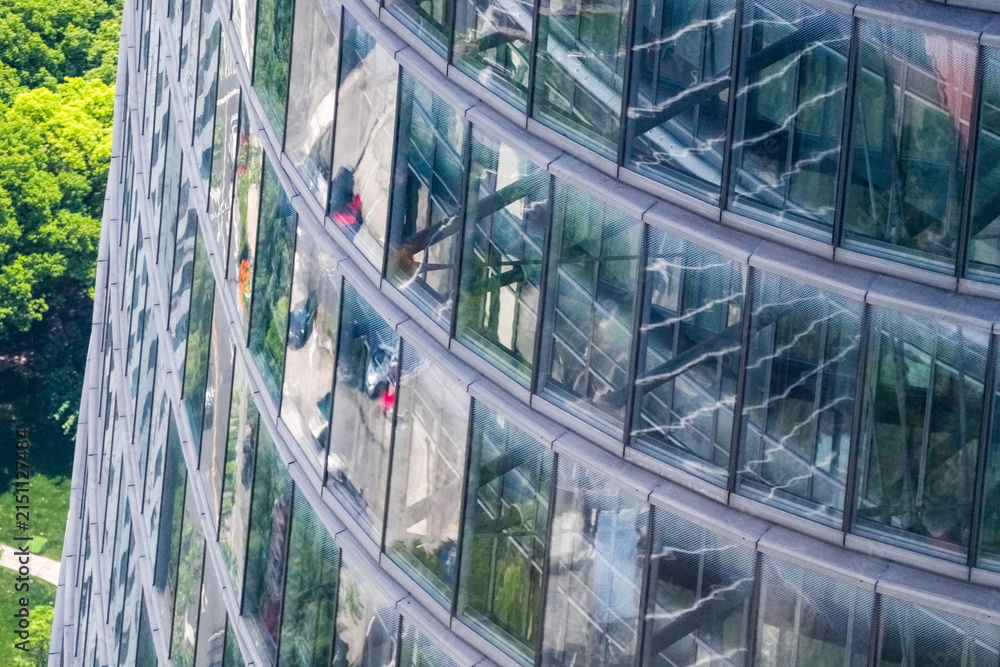 Obraz premium Aerial close view of a curved glass tower facade with occupied floors visible behind the glazing, reflections of the district sliding across the curved glass, high above the daily commute.