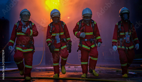 The four firefighters in protective gear walk through the remaining smoke and flames after completing an emergency response operation to extinguish a fire inside an industrial plant