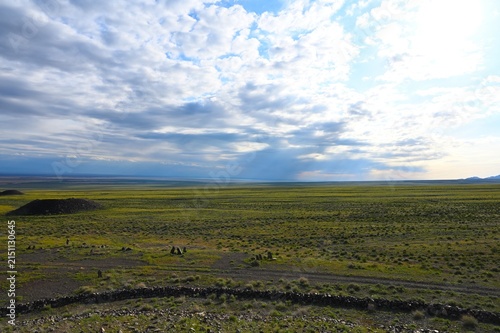 Ancient Besshatyr kurgan burial mound complex in Altyn-Emel National Park. Sacral archaeological site with stone menhirs, burial mounds and distant mountains under a blue summer sky.