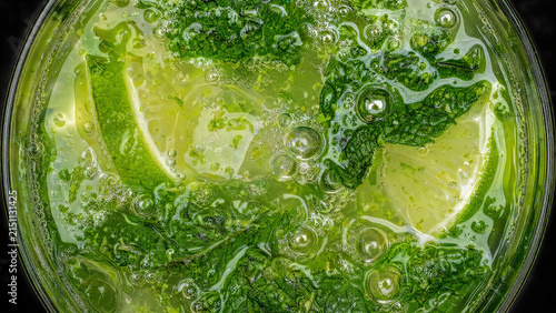 Macro top view of refreshing green mojito cocktail with mint, lime, ice and carbonation bubble