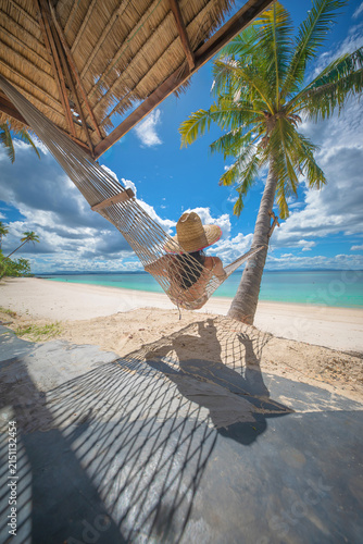 Woman tourist stay under shadow of the coconut trees at the edge of the sea beach, cheerfully traveling life in summer of the island