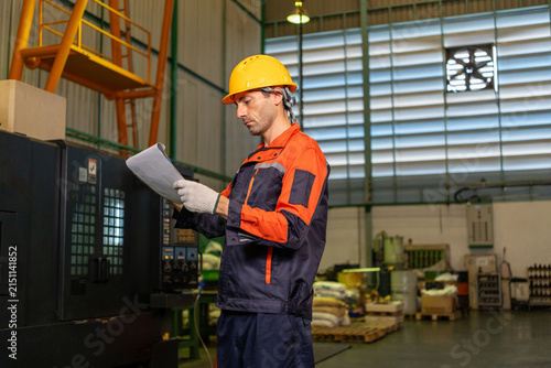 Engineer, factory, worker, helmet, safety, uniform, machine operator checks document near industrial equipment in workshop