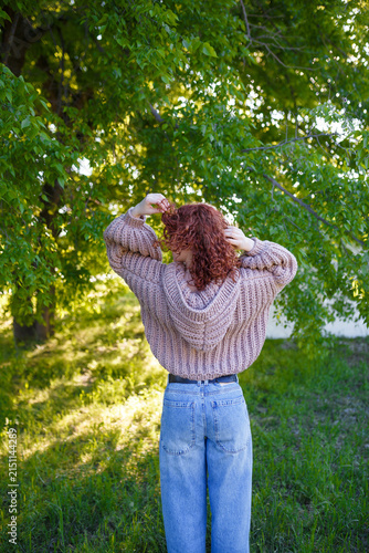Quadro su tela Redhead teenage girl in chunky knit sweater with hood back view, outdoors