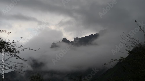 Dramatic landscape of rugged rocky mountain peaks shrouded in thick white fog and dense clouds. Majestic alpine scenery at high altitude with misty summits under an overcast sky — ideal for travel, ad