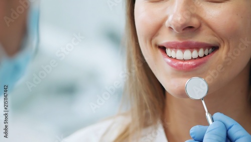 Woman smiling widely showing bright teeth during dental examination with dentist using mirror tool