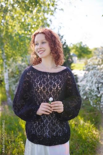 redhead teenager girl in black knitted sweater posing at white blossoming bush. Model on spring background