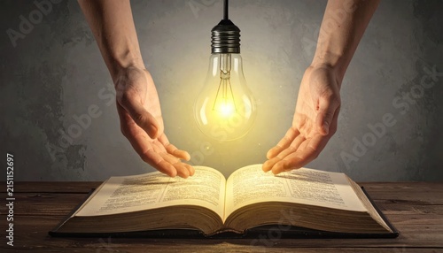 Light bulb shining over open book with human hands.