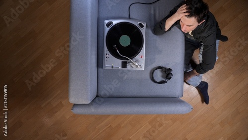 Bild auf Leinwand Man sitting on the floor by a turntable and couch, listening to vinyl records th