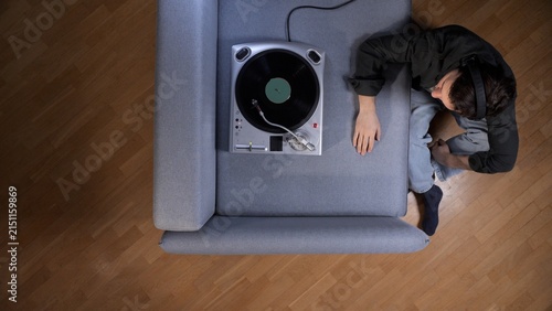 Fotografie Young man wearing headphones and relaxing on a sofa, listening to music from a v