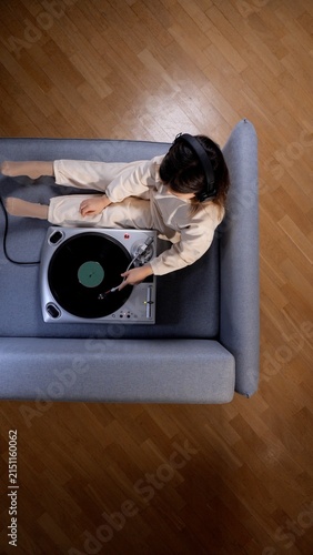Photography Young woman relaxing on a gray couch, wearing headphones and carefully placing t