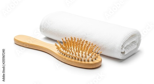 A bamboo hairbrush rests on a white towel. The brush has many bristles and a wooden handle.