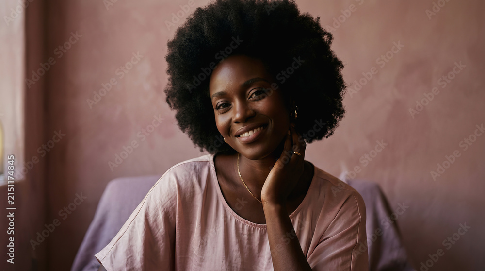 Fototapeta premium Smiling young woman with afro hairstyle resting her chin on hand in a softly lit room