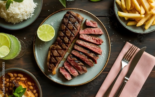 Grilled steak slices with lime on rustic plate beside crispy fries and fresh sides
