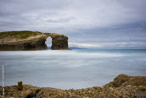Moody long exposure of misty sea and rock at Praia das Catedrais, Beach of the Cathedrals in Ribadeo, Galicia Spain