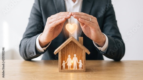 Businessman hands protecting wooden house model with glowing heart symbol, representing home insurance policy, family security and property protection concept