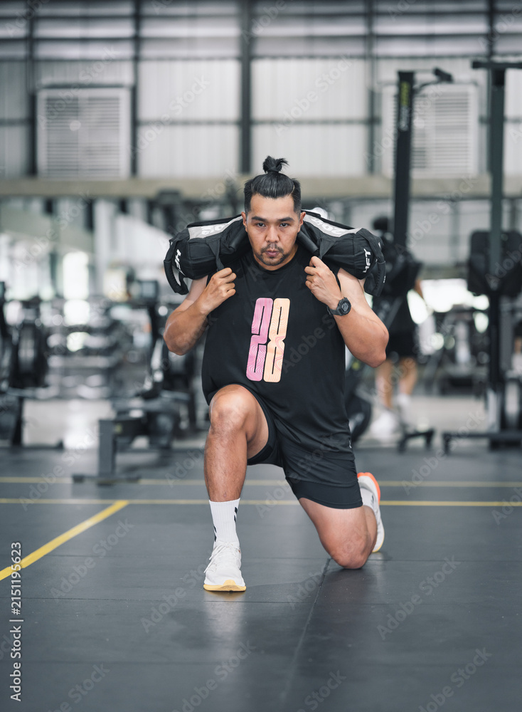 Fototapeta premium Man doing lunges with weighted bag in gym