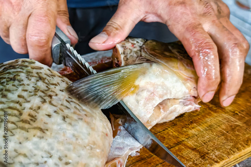 Принти на полотні A person cuts a fish on a wooden surface in a kitchen