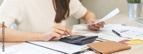 Stressed asian young business woman, employee using calculator to calculate expenses of monthly, hand holding bills and receipt for to payment on table at home. Financial, finance of banking concept.