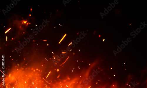 Fiery sparks and embers rising against a dark black background dramatic illumination
