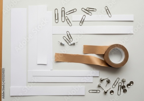 Office Supplies Arrangement: An organized collection of essential office supplies, including paper clips, pushpins, tape, and white paper strips.