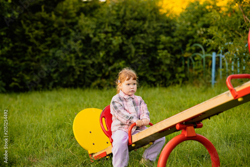 Little girl playing on a seesaw at the park. Child having fun on a playground in nature. Outdoor activity for children, recreation and healthy childhood development concept.