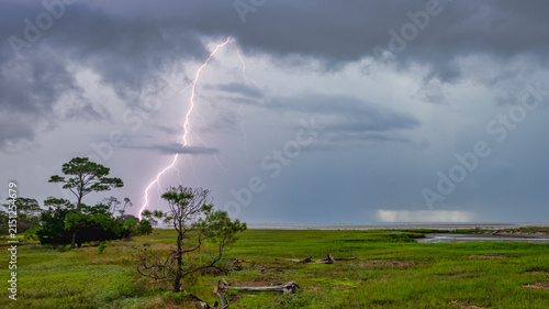 Fotografie Lightning strikes over a marshland during a stormy evening in a coastal area