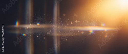 Lens flare with golden dust particles and anamorphic rainbow prism light streaks on a dark background, creating a cinematic lighting overlay for video editing and photography