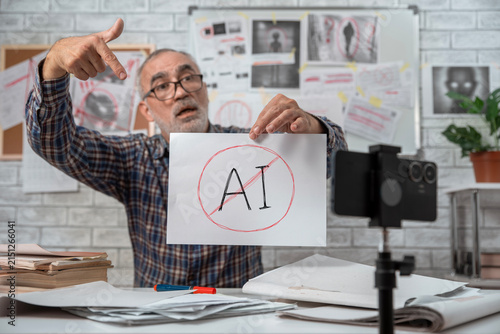 Fotografie Senior conspiracy blogger pointing at a crossed out AI sign while recording an e