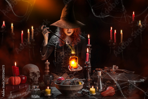 Quadro su tela Witch with a magic wand casts a spell, conjuring a love potion, a bottle with glowing poison in her hands