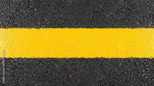Bright yellow line painted on dark asphalt road surface creating a contrasting abstract background texture with a rough granular pattern