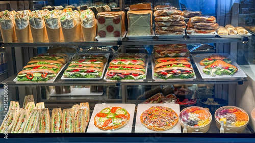 Brightly lit gourmet deli display in a modern cafe showcasing sandwiches pizzas and salads in a glass case suitable for restaurant menus, food blogs, social media
