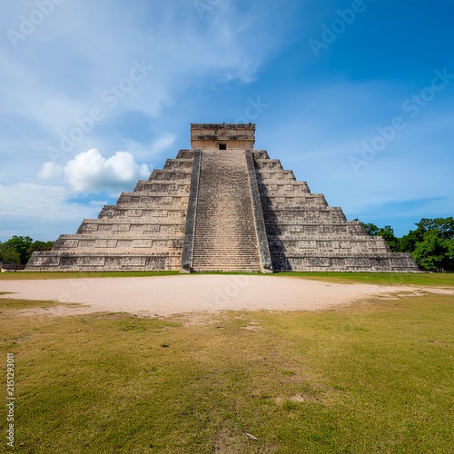 Ancient stone temple ruins on grassy plain under blue sky.