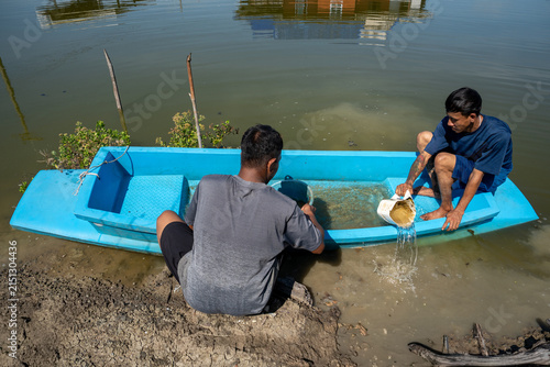 Fotografie Friends working together to bail water from small rowboat on pond