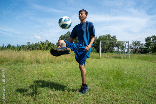 Asian soccer player juggling football in mid-air on grass field. Action photo of a young man juggling a football high off the ground during outdoor training.