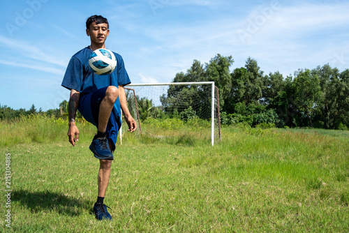 Asian soccer player juggling football in mid-air on grass field. Action photo of a young man juggling a football high off the ground during outdoor training.